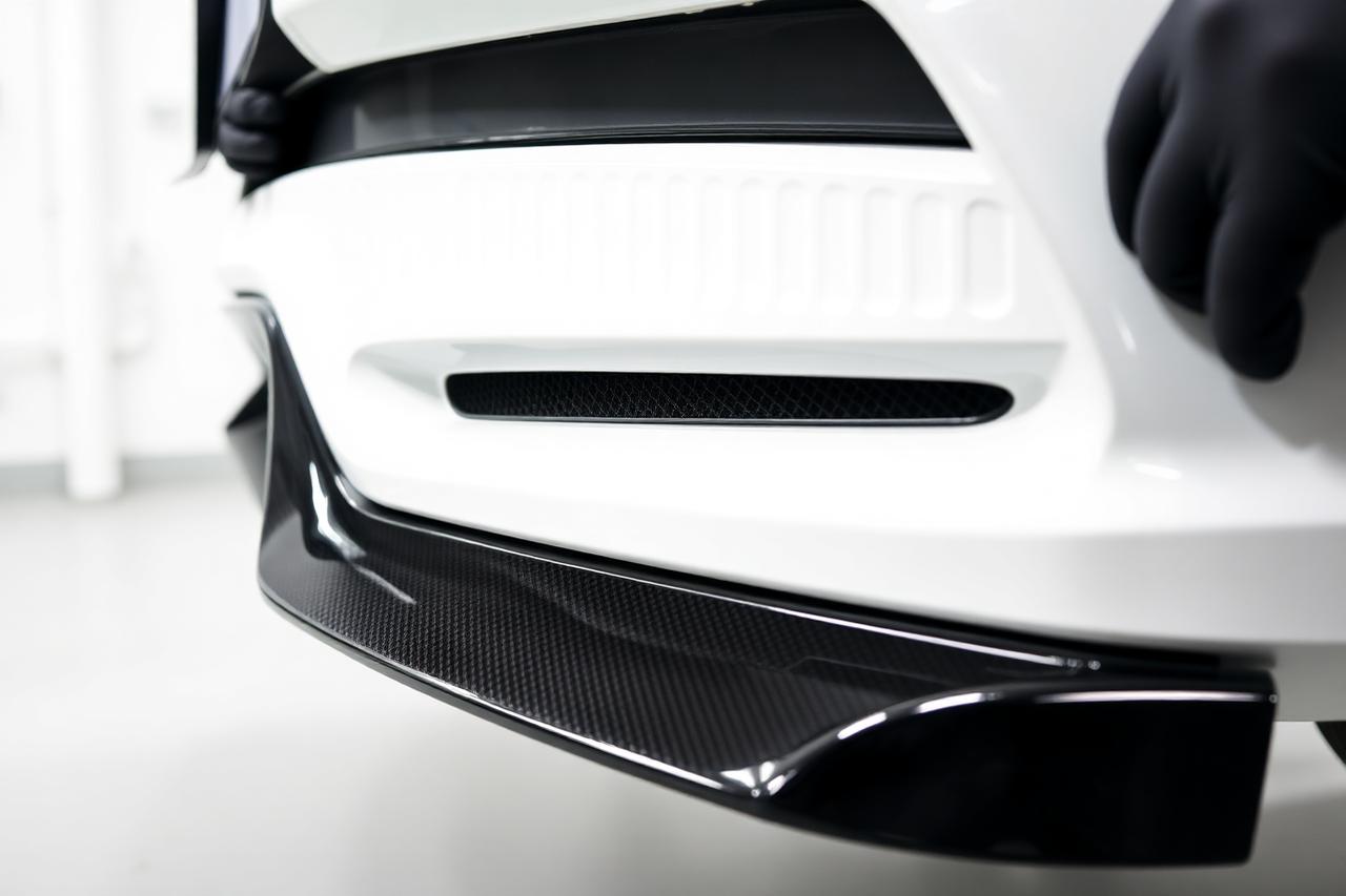 Technician fitting a gloss black front lip spoiler to a car bumper